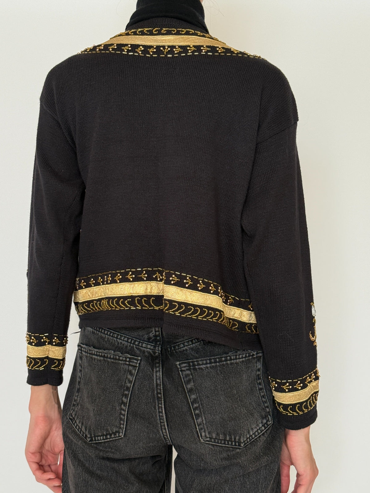 Back view of black cardigan with gold trim at hem and cuffs