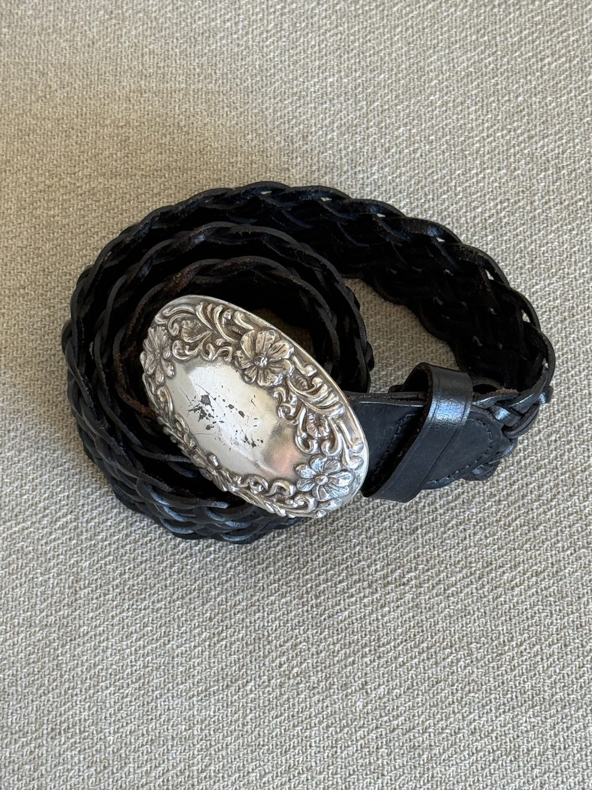 Angled view of floral silver-tone oval belt buckle and black leather