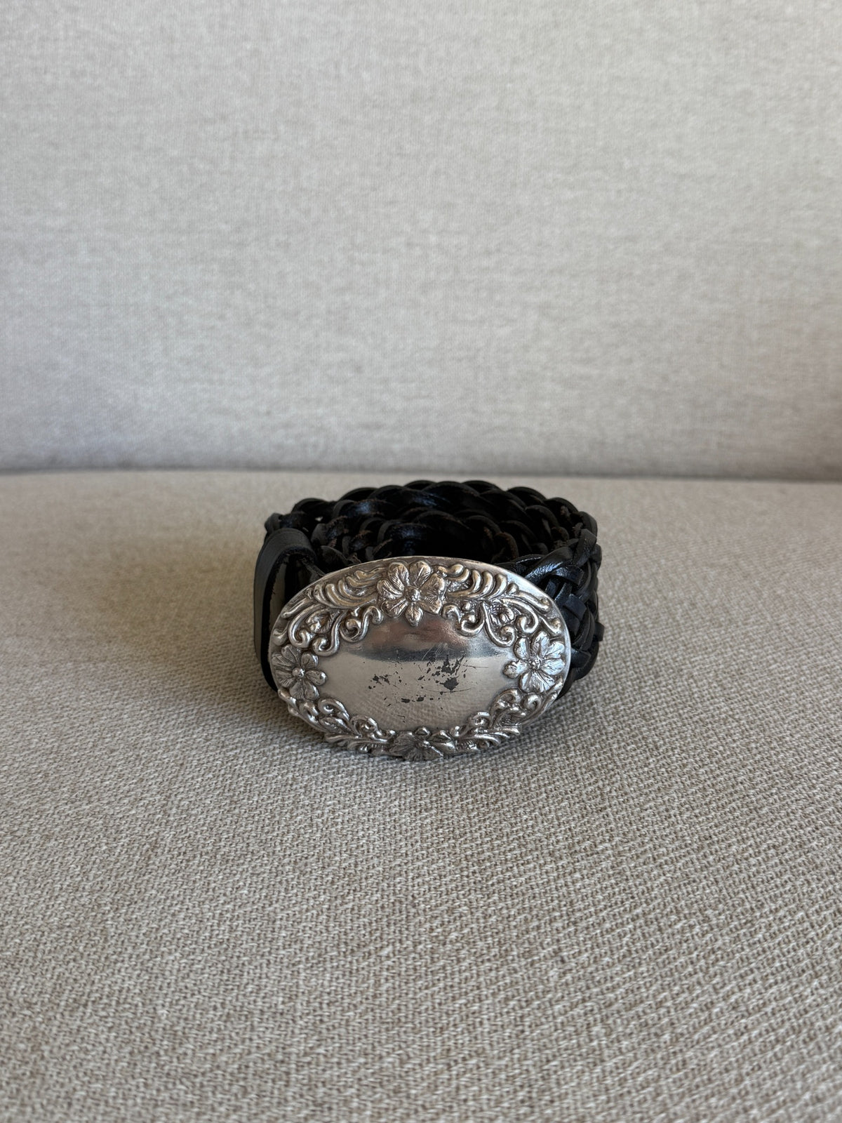 Front view of vintage black braided leather belt with ornate silver-tone floral buckle